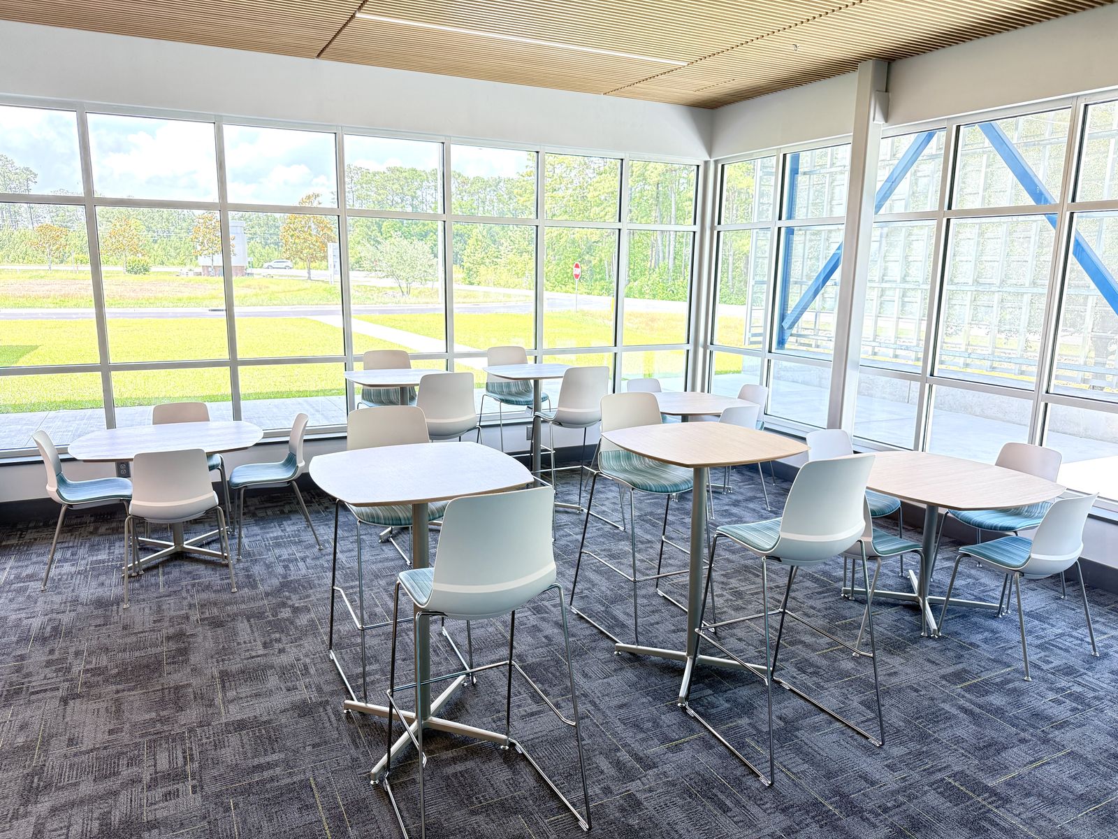 Sunlit commons with café tables and white shell chairs along a window wall