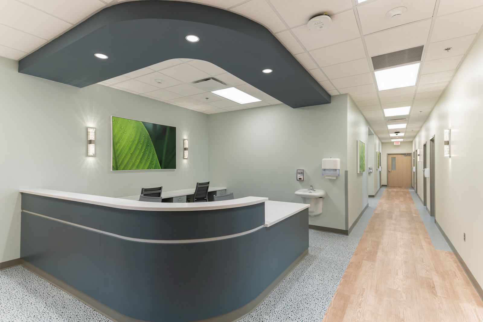Curved nurse station under a dark soffit with a long corridor beyond